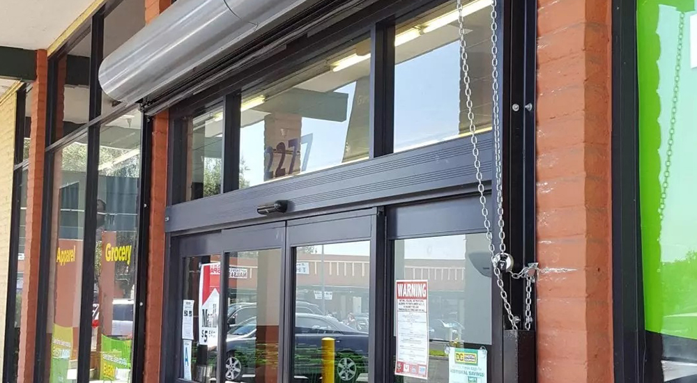 Automatic sliding glass doors at the entrance of a store, with warning and information signs posted on the glass.