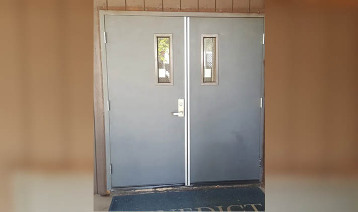Gray double doors with small rectangular windows, metal handle, and a partial floor mat visible in front.